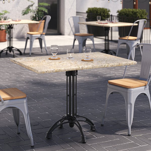 An Art Marble Furniture Kashmir White Granite Tabletop on a black metal table with a chair outside on a brick surface.