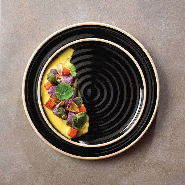 A Chef & Sommelier black stoneware dinner plate with food on it.
