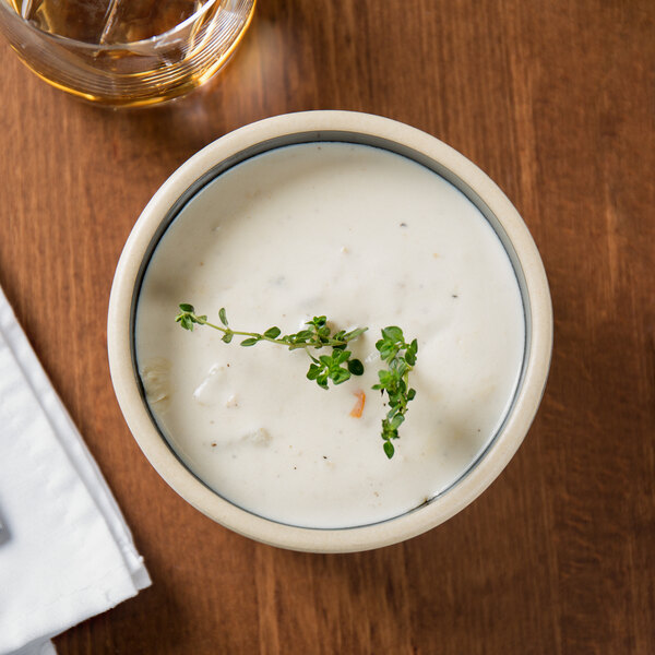 A stackable black stoneware bowl of soup with a sprig of thyme.