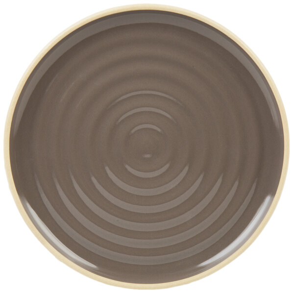 A brown stoneware plate with a white ripple design around the rim.