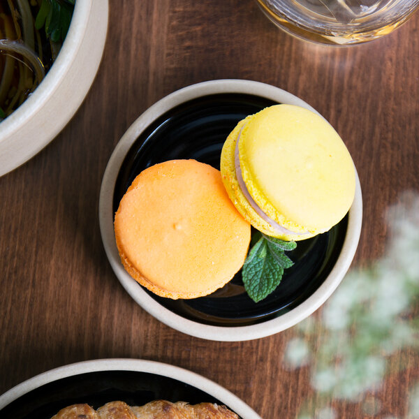 A yellow macaroon and white macaroon on a black Chef & Sommelier Geode plate.