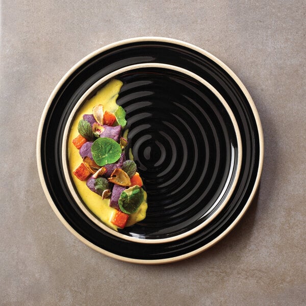 A Chef & Sommelier black stoneware plate with food on it.