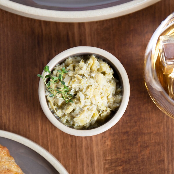 A stack of gray Chef & Sommelier Geode stoneware ramekins on a table with a bowl of food.