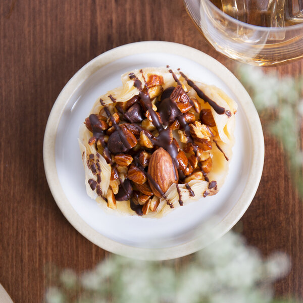 A Chef & Sommelier white stoneware plate with a chocolate covered pastry on a table.