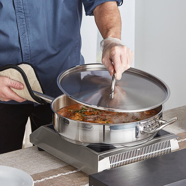 A person cooking food in a pan on a stove using a Vigor SS1 Series stainless steel lid.