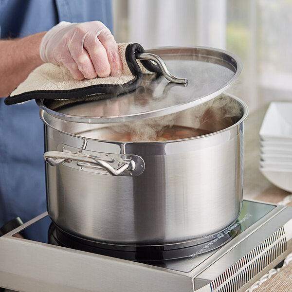 A person wearing a glove cleaning a Vigor stainless steel sauce pot on a stove.