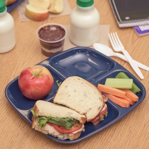 A Carlisle blue 4 compartment tray with a sandwich, apple, and vegetables.