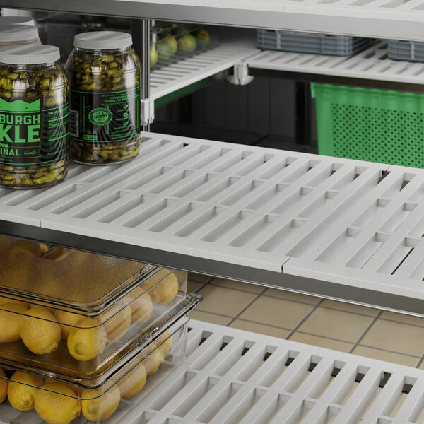 A white Cambro vented shelf with a variety of food items on it, including a jar of pickles, beans, and a lemon.