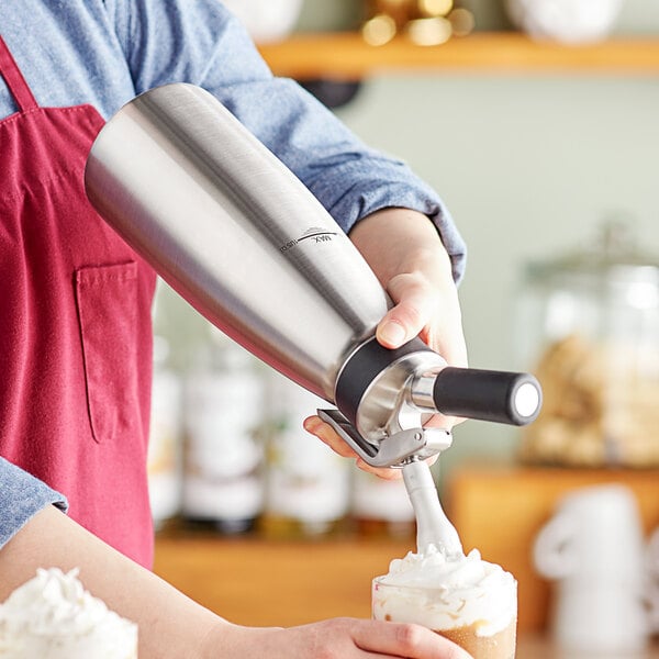Barista dispensing whipped cream from a whipped cream canister onto a latte