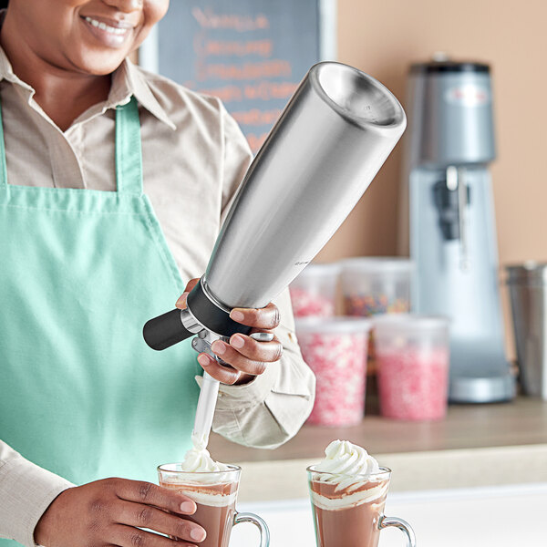 A woman using an iSi stainless steel whipped cream dispenser to top a drink with whipped cream.