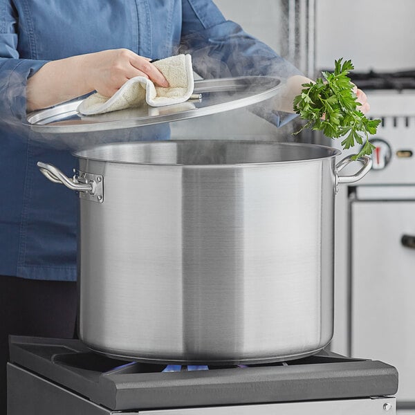 A woman using a Vigor stainless steel lid on a large pot on a stove.
