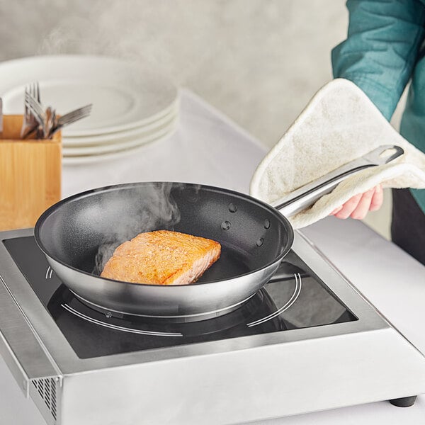 A person cooking salmon in a Vigor stainless steel non-stick fry pan.