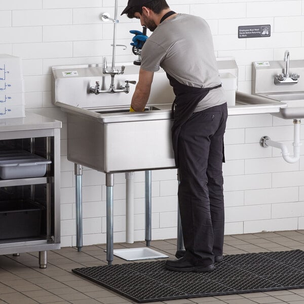A man in an apron washing dishes in a Regency stainless steel sink with a right drainboard.