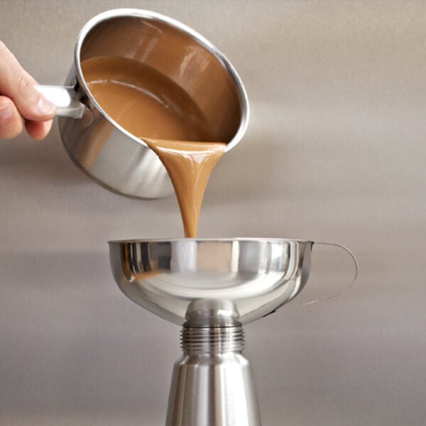 A person using a iSi stainless steel funnel to pour liquid into a silver pot.