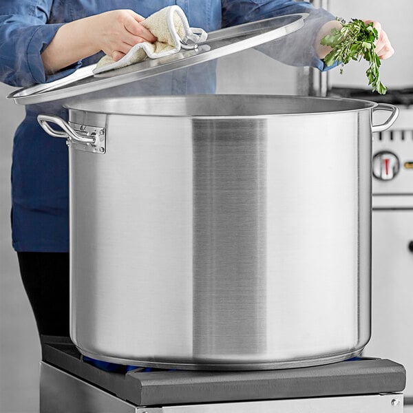 A woman using a white towel to cover a large pot on a stove.