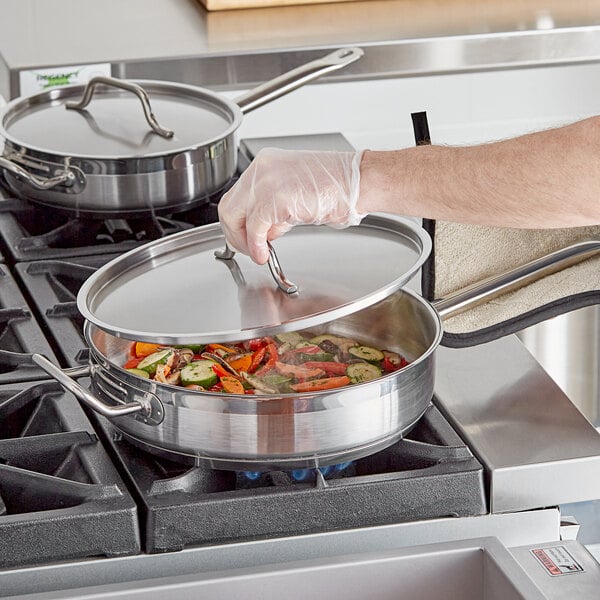 A person's hand using a Vigor stainless steel lid to cover a pot of food.