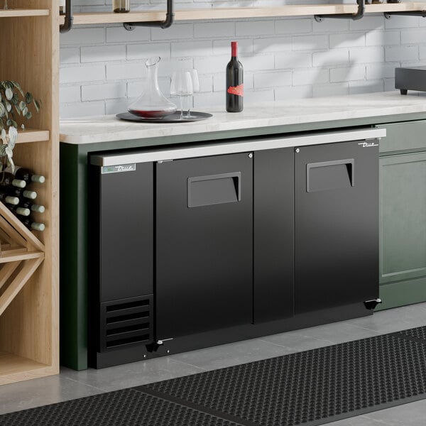 A black solid door back bar refrigerator with LED lighting installed under a countertop.