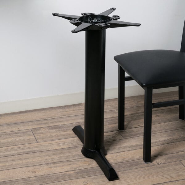 T-shaped black steel table base with spider and black chair on wood floor