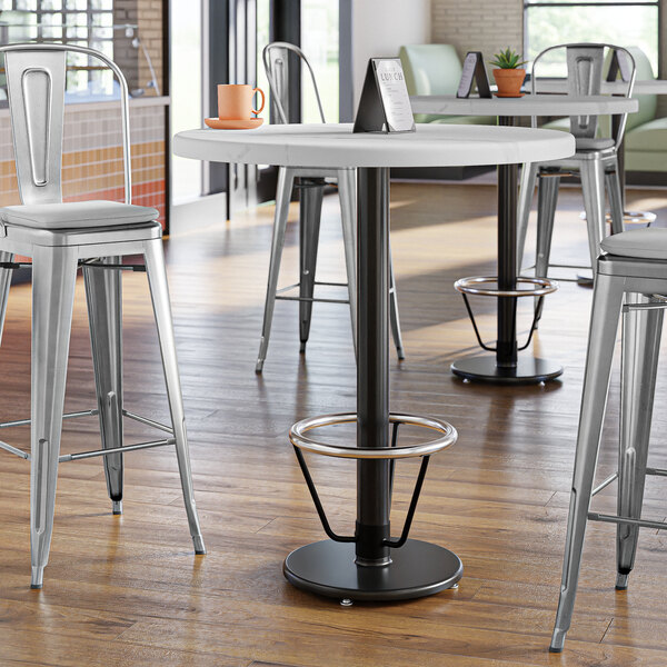 A Lancaster Table & Seating black cast iron bar height table base with a foot ring on a white table with metal legs.