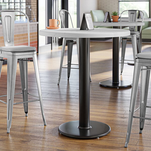 A Lancaster Table & Seating black cast iron bar height table base with a table and stools in a room.