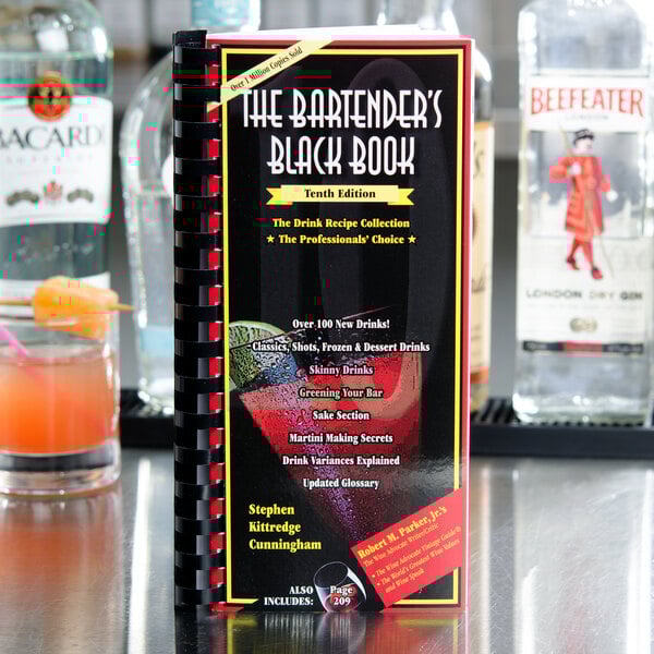 The Bartender's Black Book on a counter in a cocktail bar with a black menu.