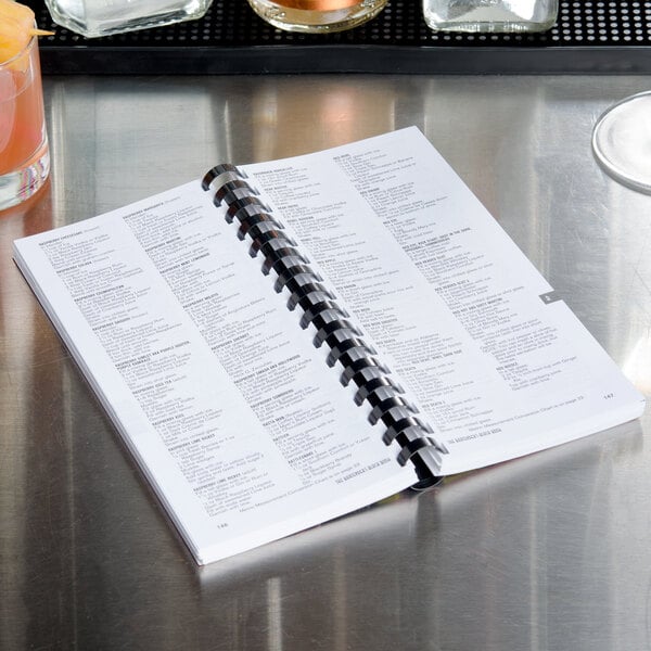 The Bartender's Black Book on a bar counter with a drink.