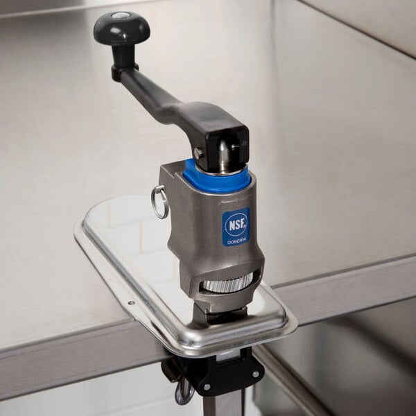A heavy-duty can opener with a long handle mounted on a stainless steel countertop.