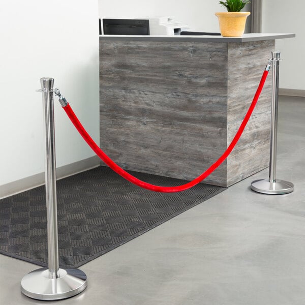 A Lancaster Table & Seating silver rope-style crowd control stanchion with red rope tied to it.