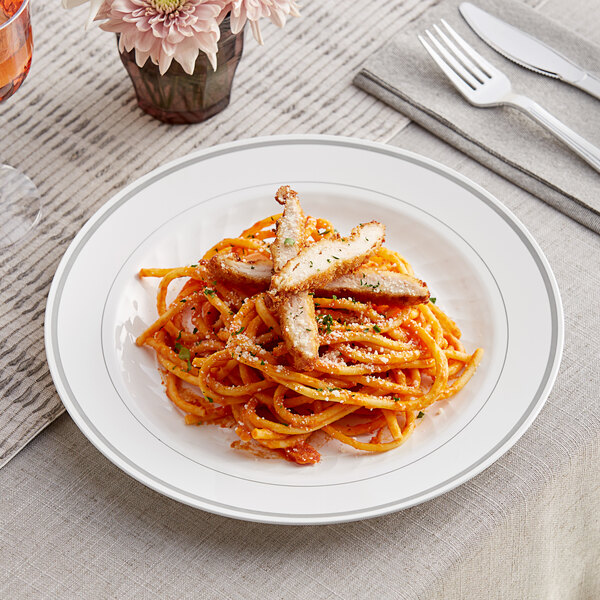 A WNA Comet white plastic plate with silver accent bands holding pasta with meat and sauce with a fork and knife on a napkin.