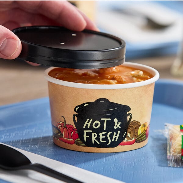 A hand holding a Choice paper soup container with food inside.