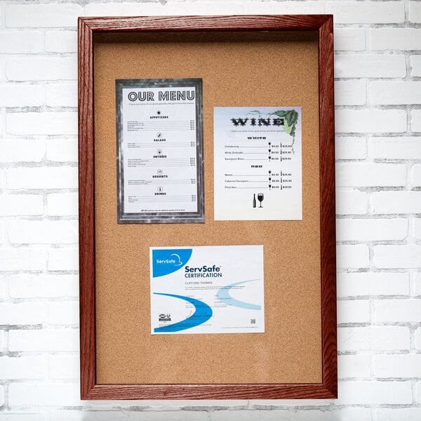 A cherry wood enclosed bulletin board with a cork board interior holding a framed menu and business card.