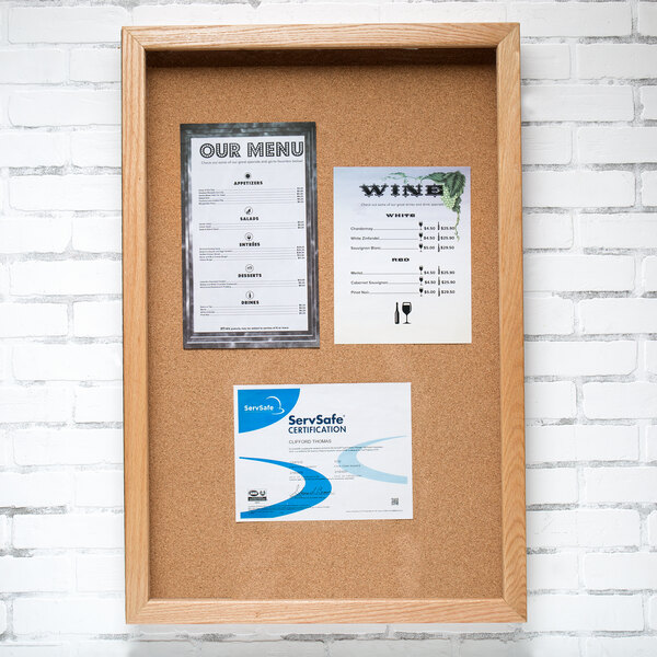 An Aarco natural oak enclosed cork board with a menu on it.