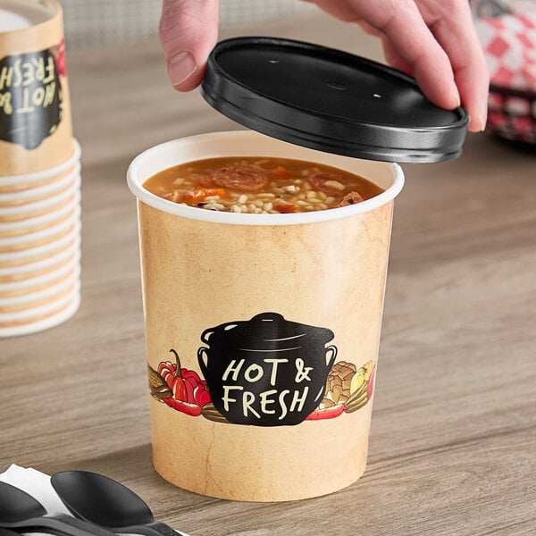 A hand holding a Choice paper soup cup with a vented paper lid filled with soup.