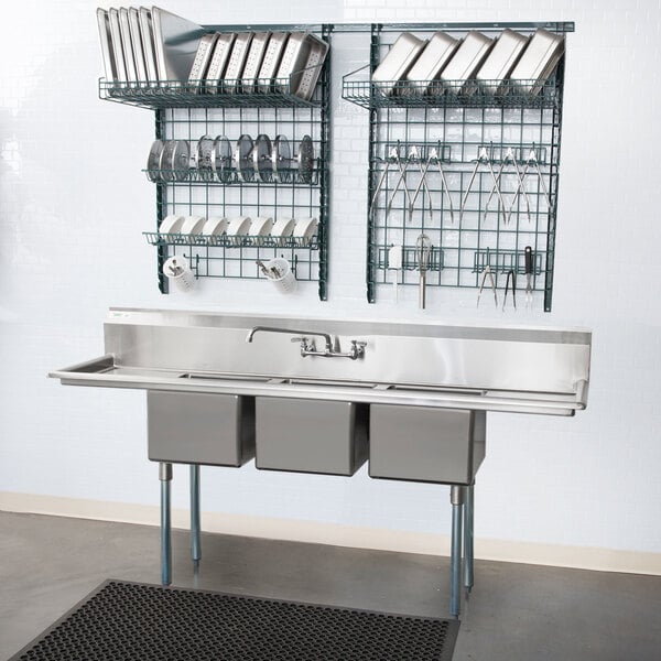 A Metro SmartWall G3 dish wash task station with metal containers and utensils on a wall above a sink.