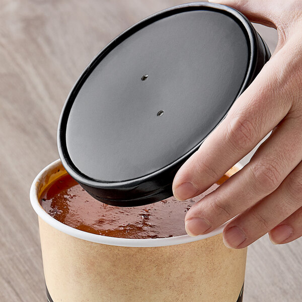 A hand holding a black lid over a container of food.