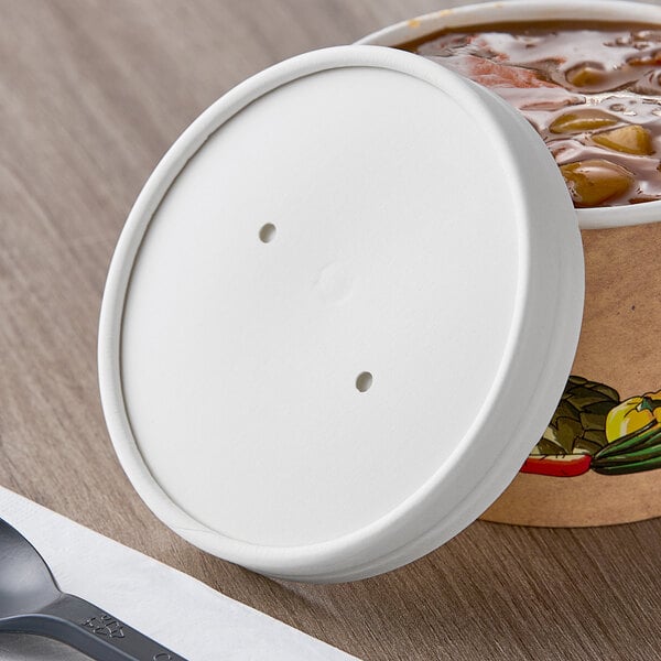 A white paper soup container with a white vented lid on top of a table with a plastic spoon.