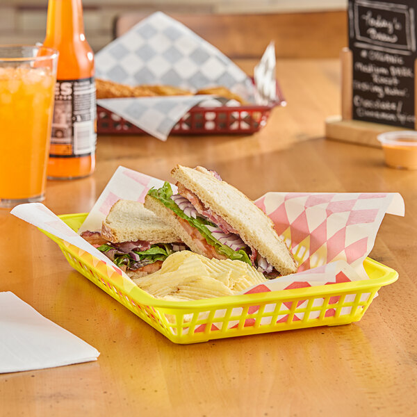 A yellow rectangular plastic fast food basket on a table with sandwiches and chips inside.