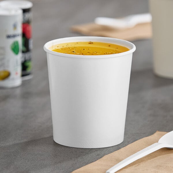A white Choice paper food cup filled with soup on a table.