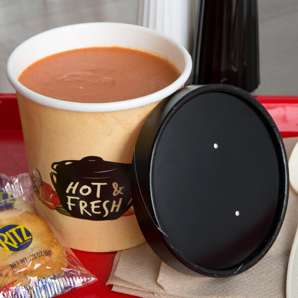 A Choice paper soup cup with a vented paper lid filled with soup on a tray with a cracker.