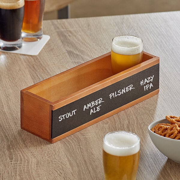 An Acopa walnut finish flight crate with a glass of beer and a bowl of pretzels on a table.
