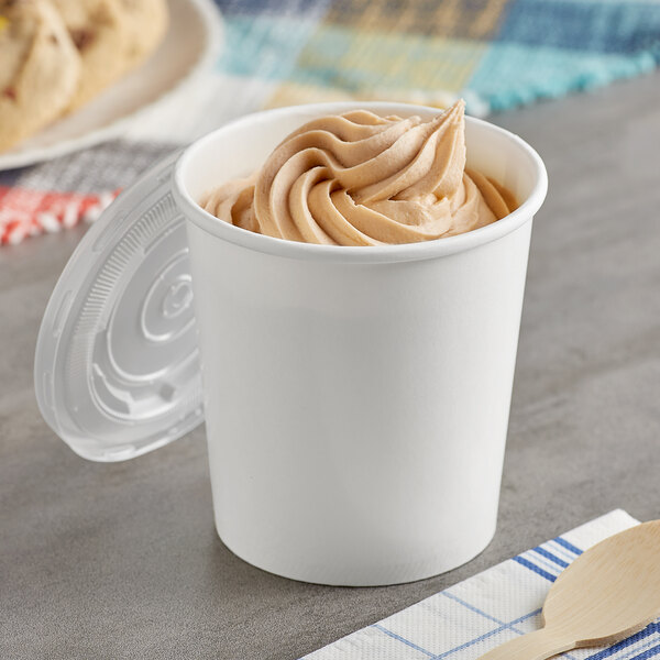 A Choice white paper food cup with a vented plastic lid filled with ice cream with a wooden spoon.