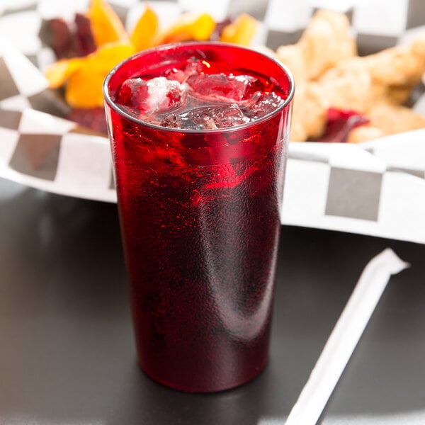 A Cambro Ruby Red plastic tumbler filled with red liquid and ice on a counter with a straw holder.