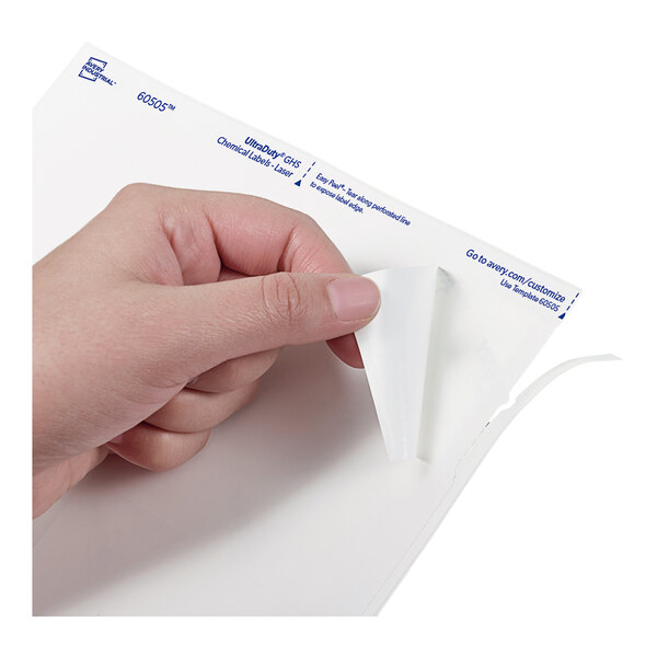 A hand is peeling a white adhesive label from a sheet with blue text in the corner.