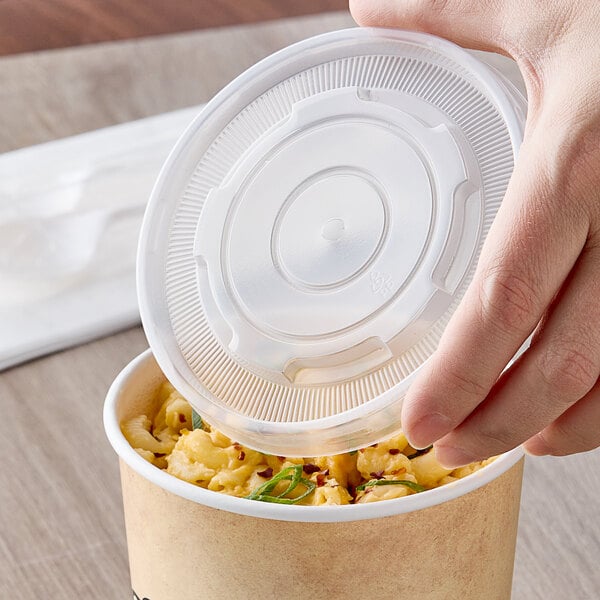 A hand holding a clear plastic lid over a bowl of macaroni and cheese.