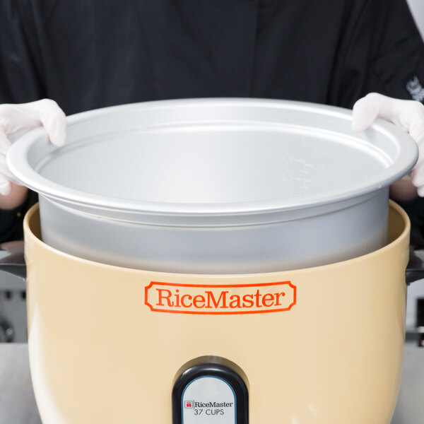 A person in gloves holding a Town rice cooker pot.