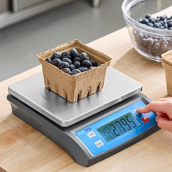 A person weighing a box of blueberries on an AvaWeigh digital scale.