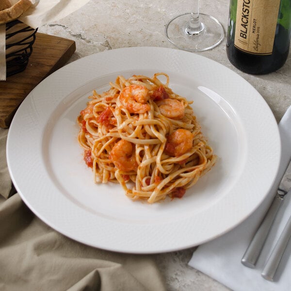 A Villeroy & Boch white porcelain flat plate with pasta, shrimp, and wine on it.