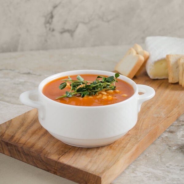 A bowl of soup with a sprig of leaves on a cutting board.