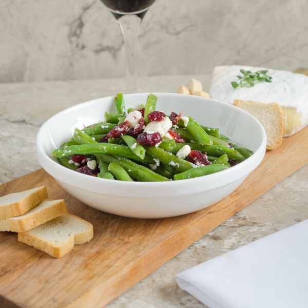 A Villeroy & Boch white porcelain bowl filled with green beans with cranberries and cheese on a cutting board.