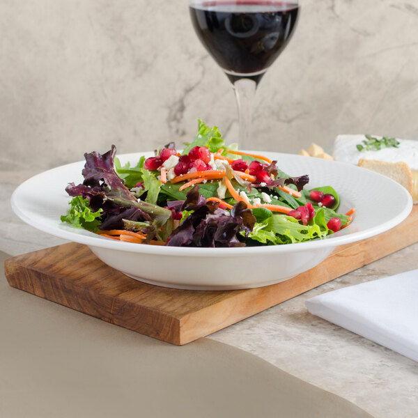A Villeroy & Boch white porcelain soup plate filled with salad next to a glass of wine.